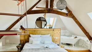 A bedroom with a large bed, a wooden headboard, a round mirror, a hanging light fixture, and a view of the bathroom. - Domaine de la Fauvrière (Sainte-Honorine-de-Ducy)