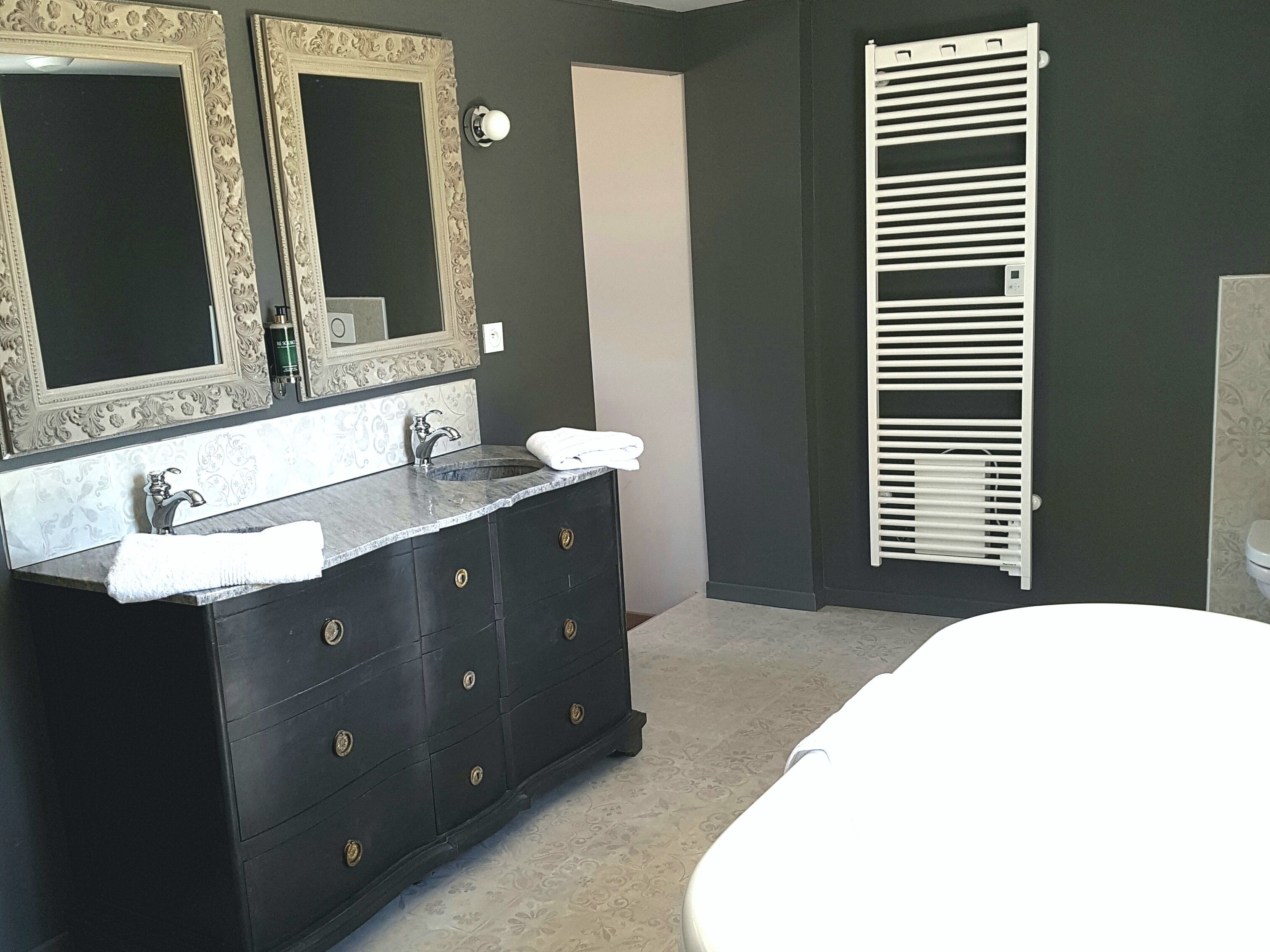 A bathroom with a dark-colored vanity, two mirrors with ornate frames, a white sink, and a white towel on the counter.