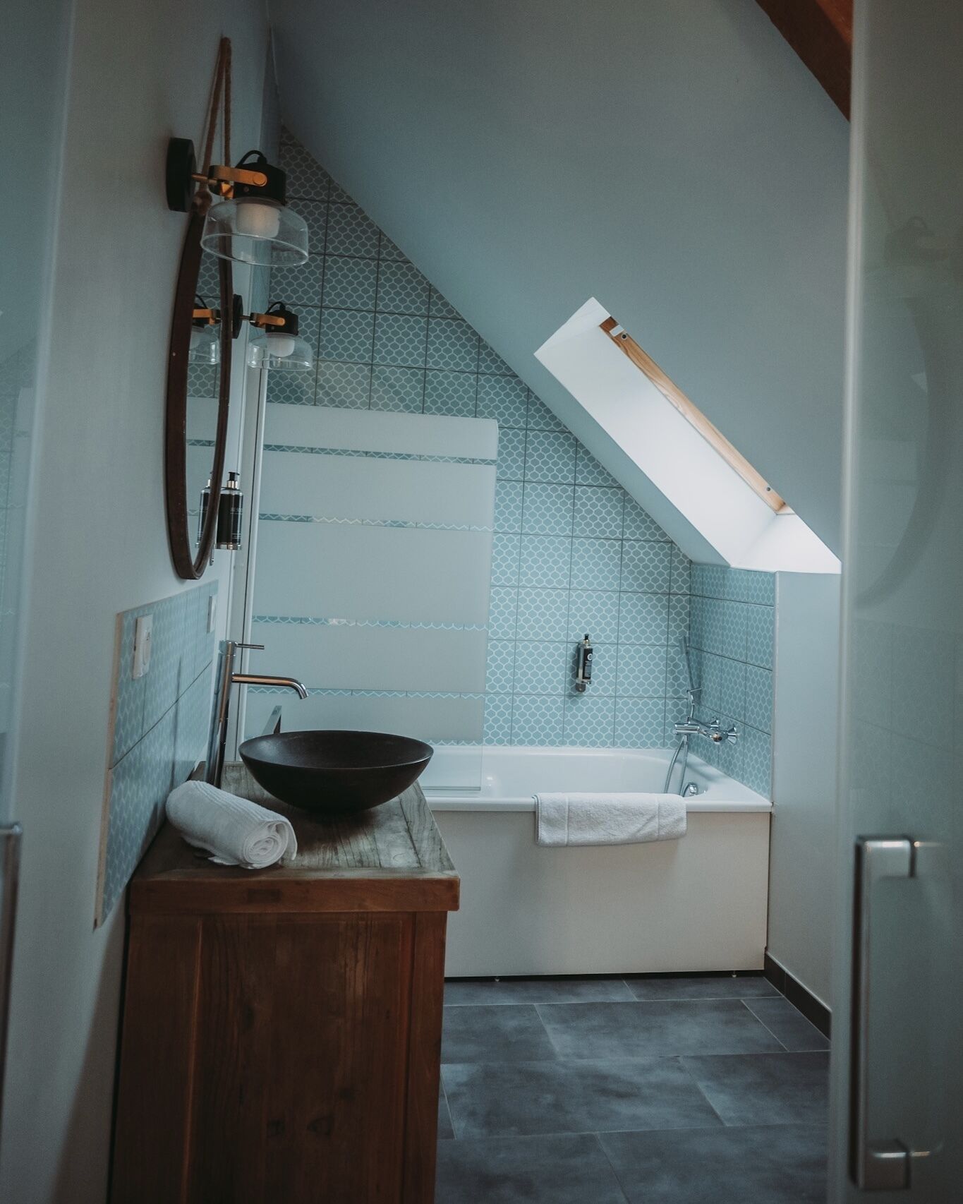 A bathroom with a bathtub, a wooden vanity, a large mirror, and a skylight.