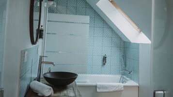 A bathroom with a bathtub, a wooden vanity, a large mirror, and a skylight.