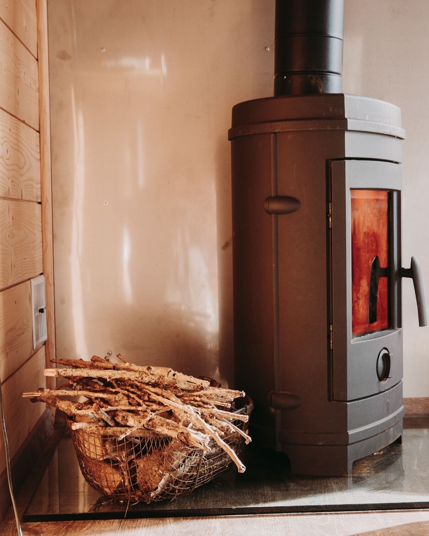 A wood-burning stove with a metal basket of firewood beside it.