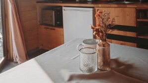 A wooden interior with a table set for dining, a vase with dried flowers, and a kitchen in the background. - Domaine de la Fauvrière (Sainte-Honorine-de-Ducy)
