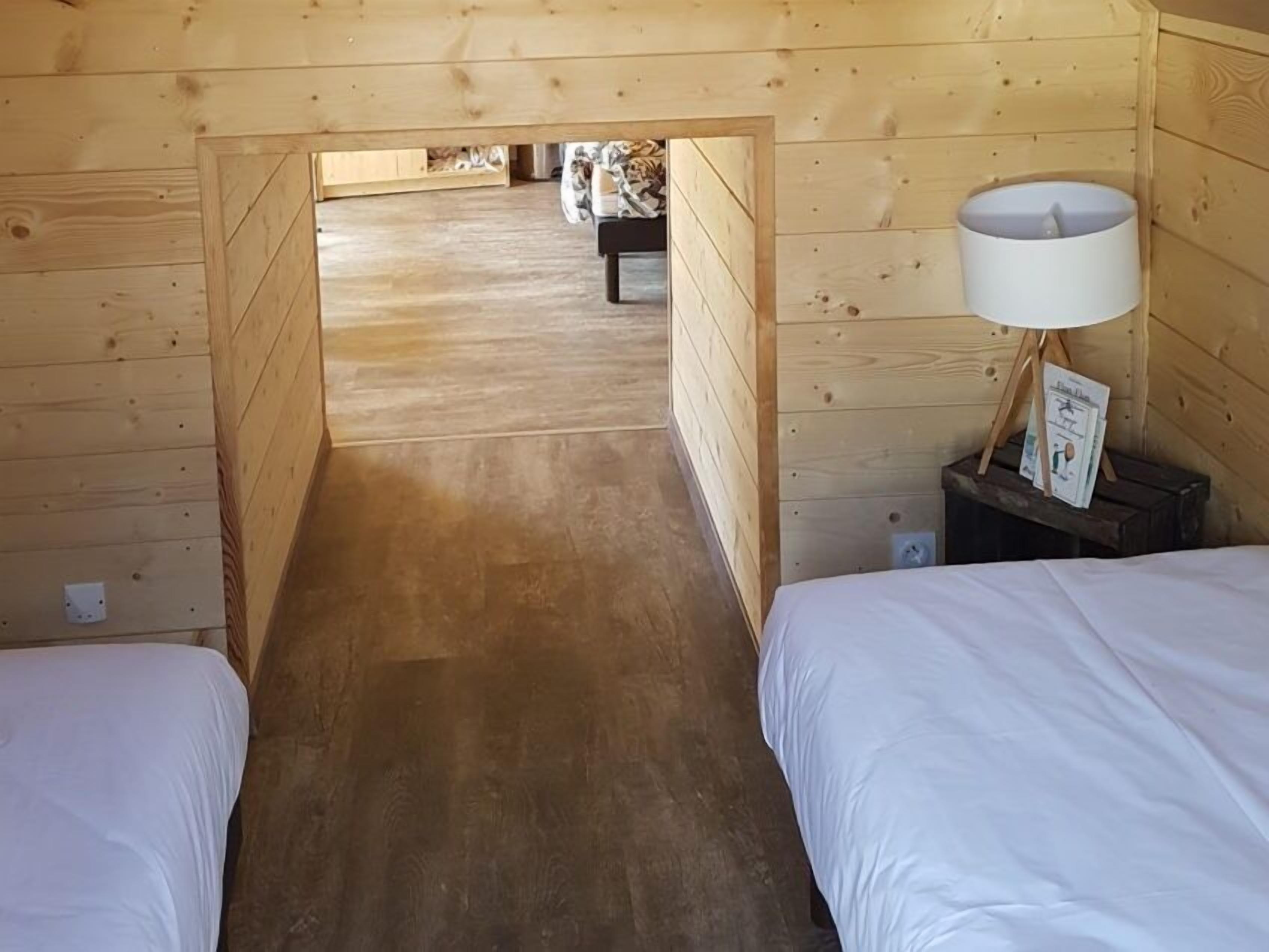 A wooden cabin room with two beds, a nightstand with a lamp, and a framed picture.