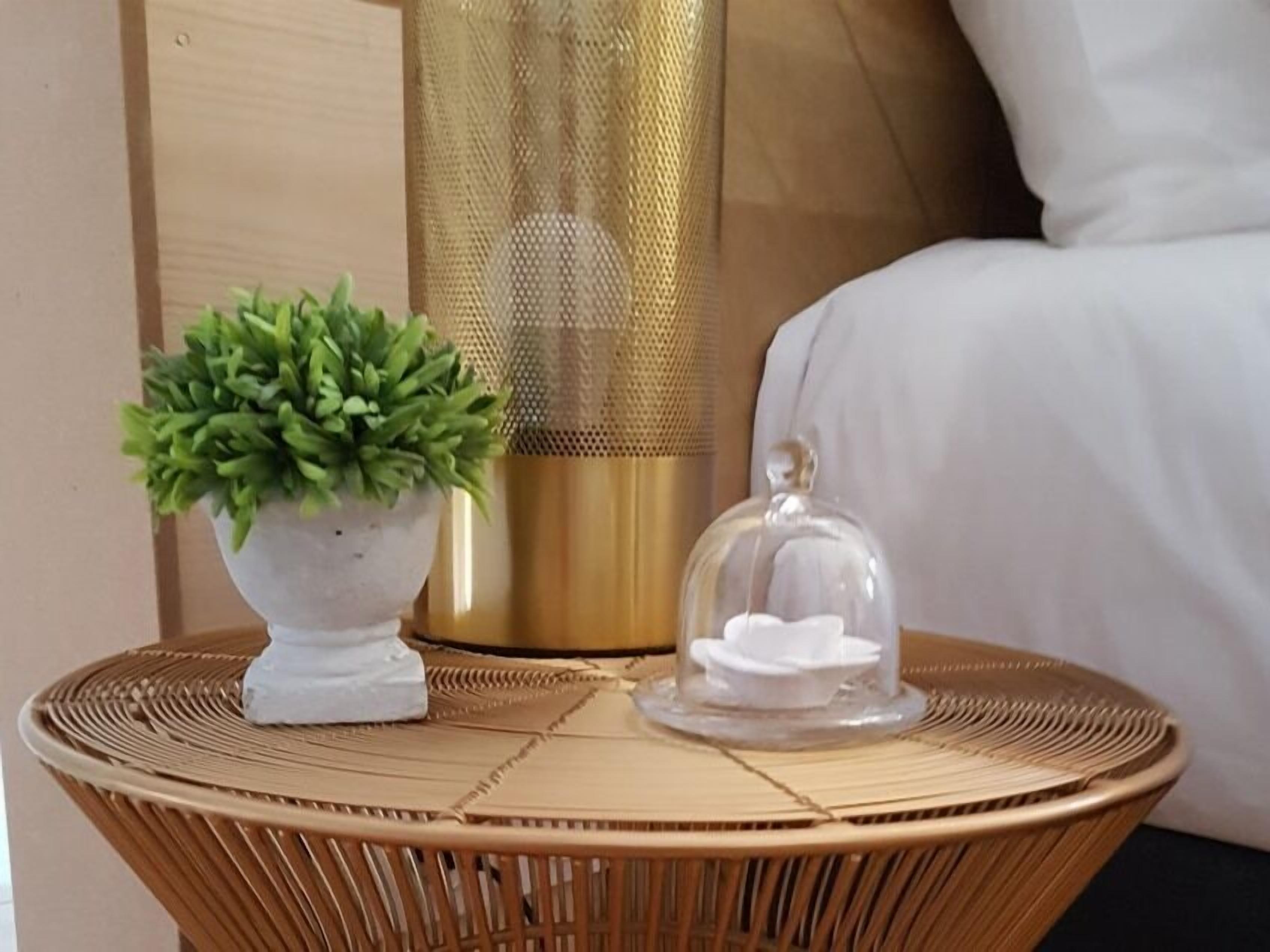 Une table ronde en osier, sur laquelle se trouve une petite plante en pot et une cloche de verre contenant un objet blanc.
