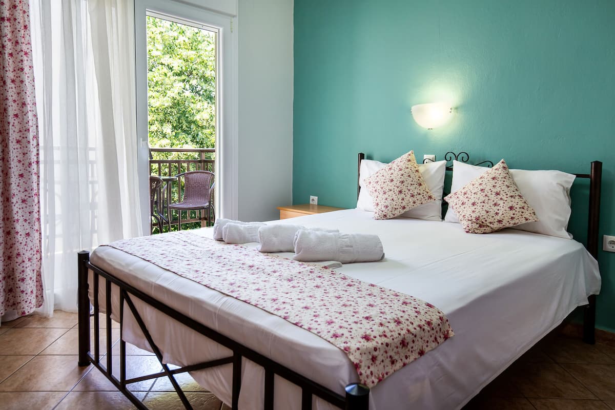 A neatly made bed with floral bedding, a teal wall, and a balcony with a chair.