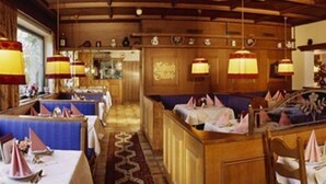 A restaurant with wooden paneling, tables set with white tablecloths and pink napkins, and hanging lamps. - Seiwald (Kirchdorf in Tirol)