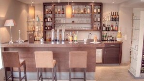 A bar area with a counter, stools, and shelves stocked with bottles and glasses. - Seiwald (Kirchdorf in Tirol)