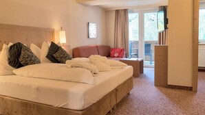 A hotel room with a large bed, a bedside table, a lamp, a red bag, and a view of the outdoors. - Seiwald (Kirchdorf in Tirol)