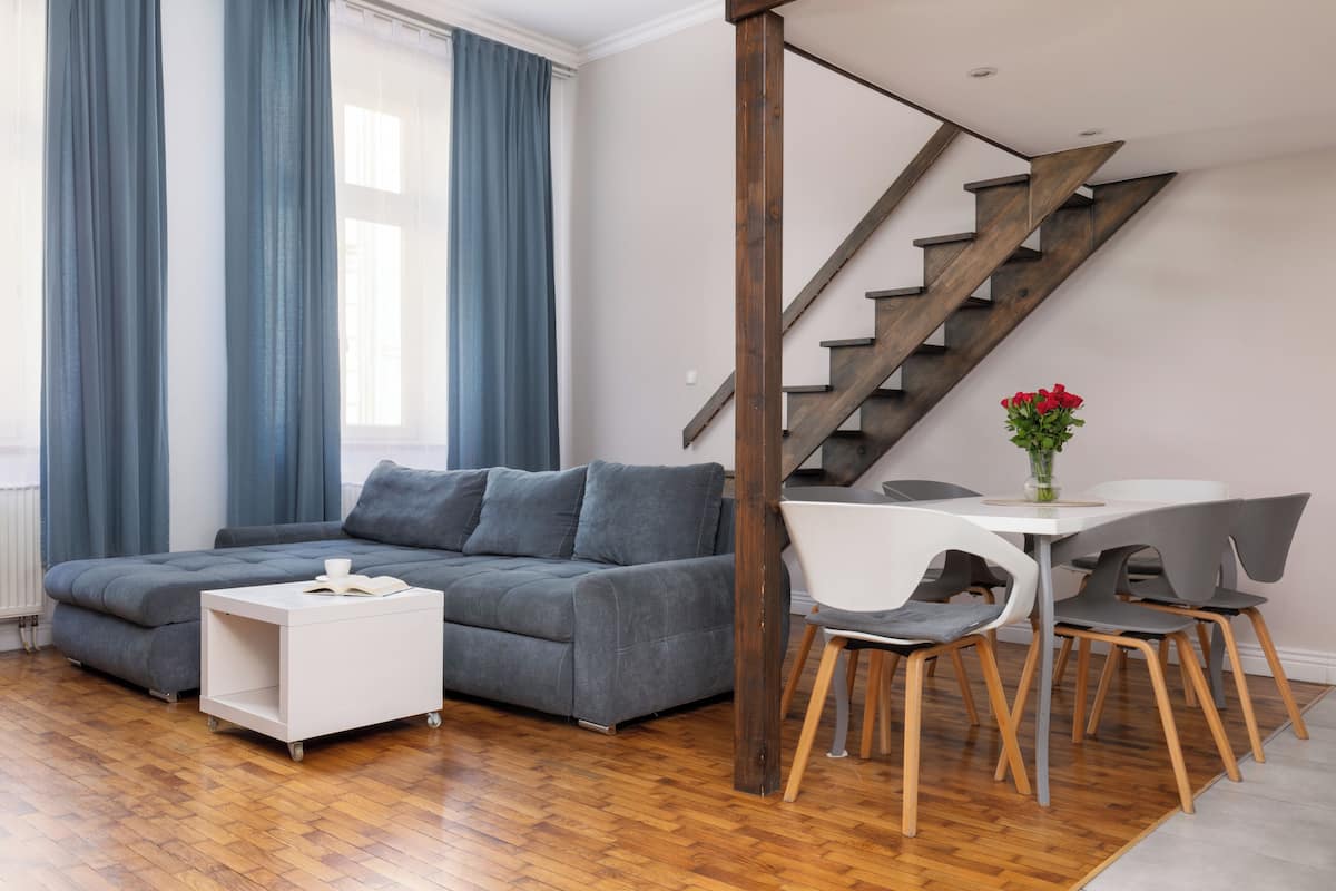 A modern living room with a grey sofa, white side table, and a dining area with a white table and grey chairs.
