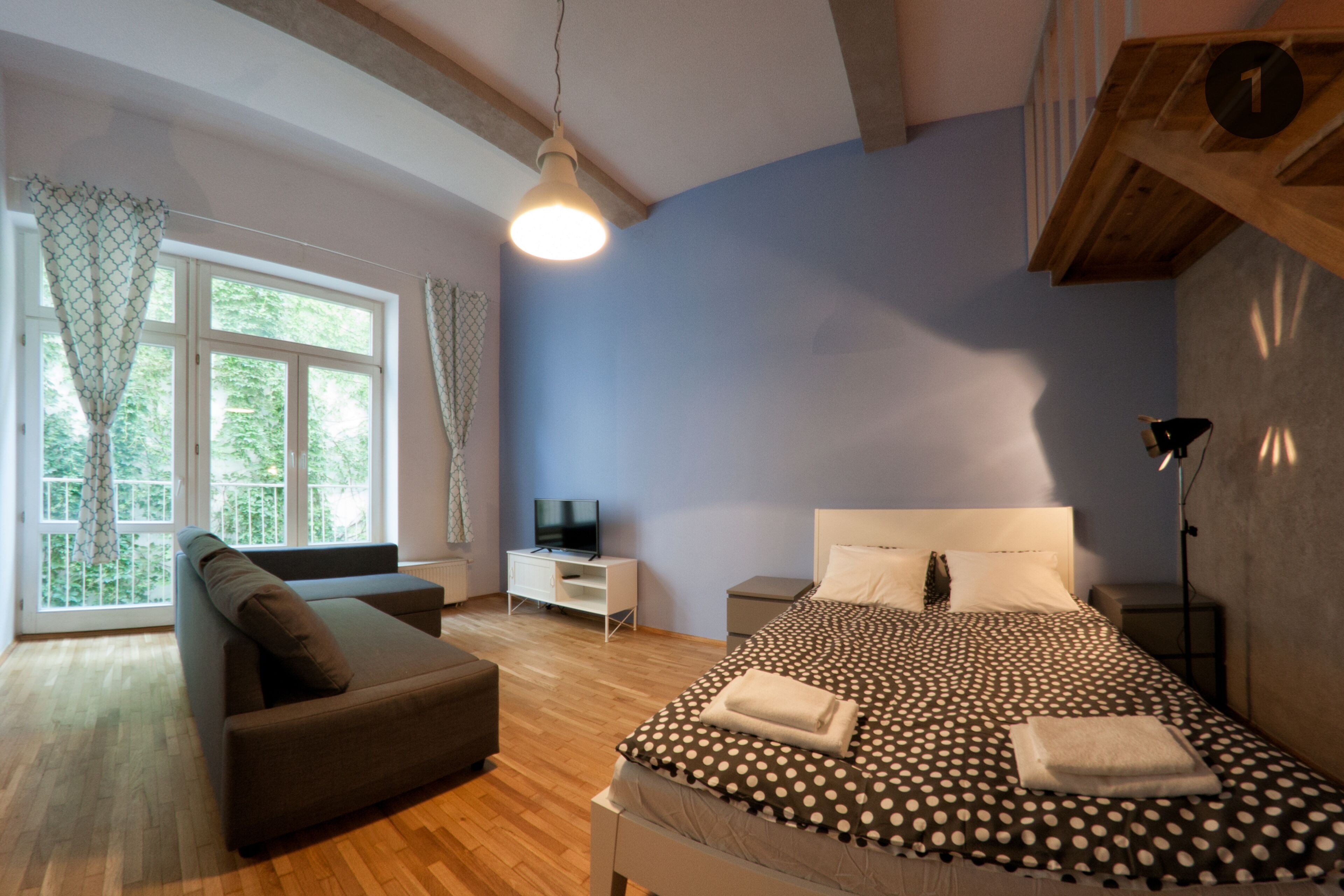 A bedroom with a bed, a sofa, a TV, and a window with curtains.