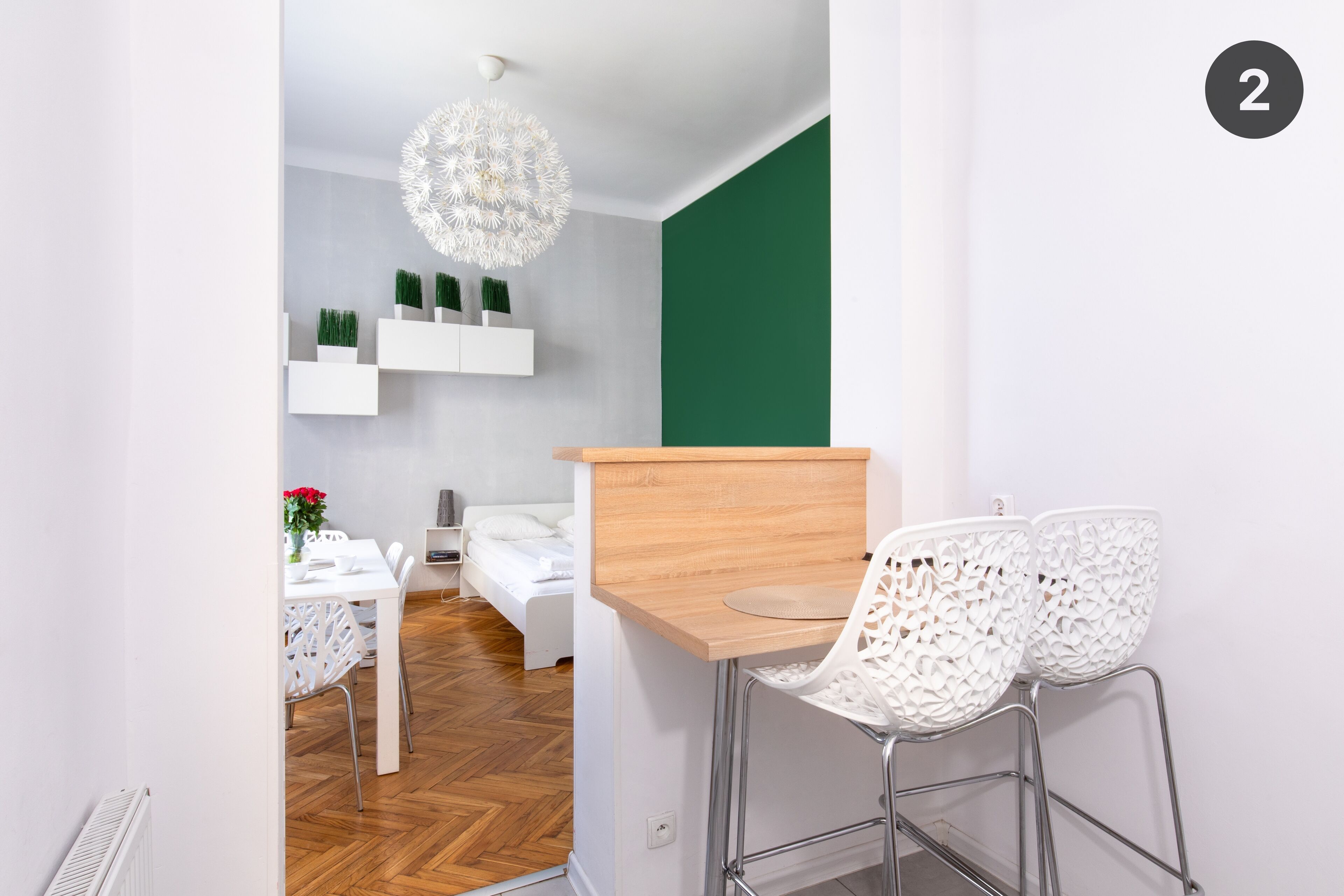 A modern room with a wooden desk, white chairs, a bed, and a green accent wall.