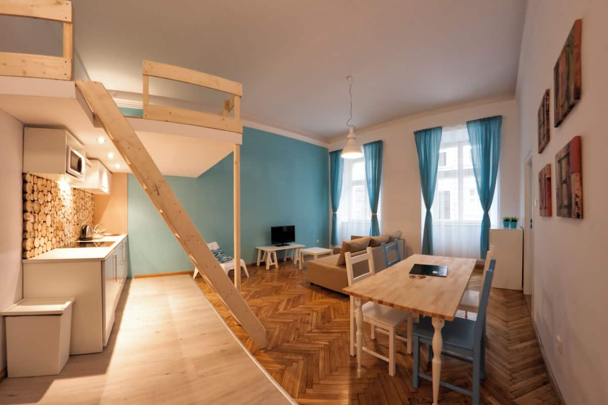 A compact living space with a kitchen, dining area, and a loft bedroom with a wooden staircase.