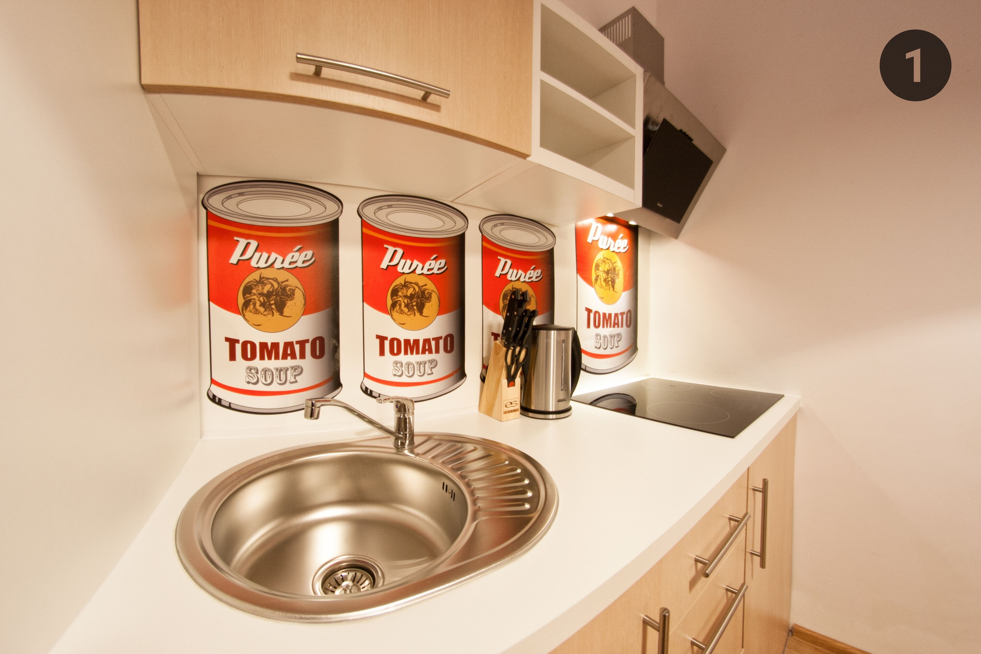 A kitchen with a stainless steel sink, wooden cabinets, and four cans of Purée Tomato Soup.