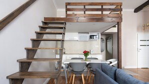 A modern kitchen with white cabinets, a microwave, and a dining area with grey chairs and a table. - Fresh Apartments (Kraków)