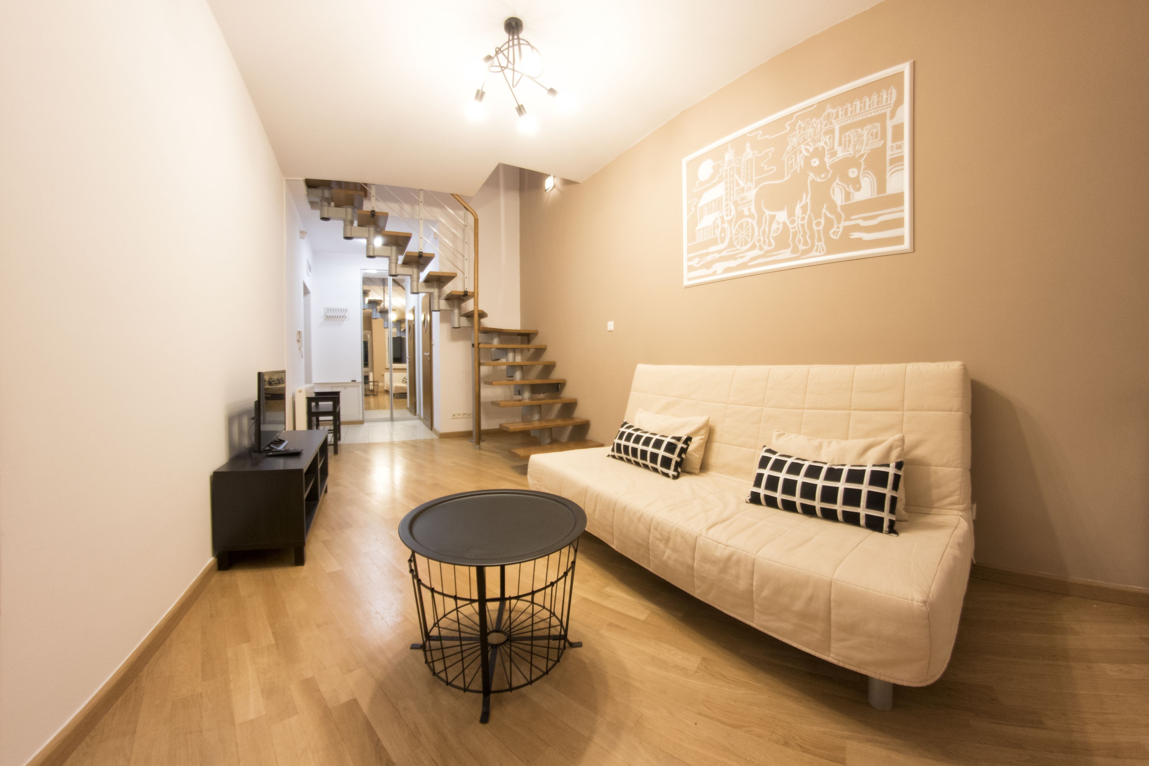 A modern living room with a sofa, a round coffee table, and a staircase leading to another level.