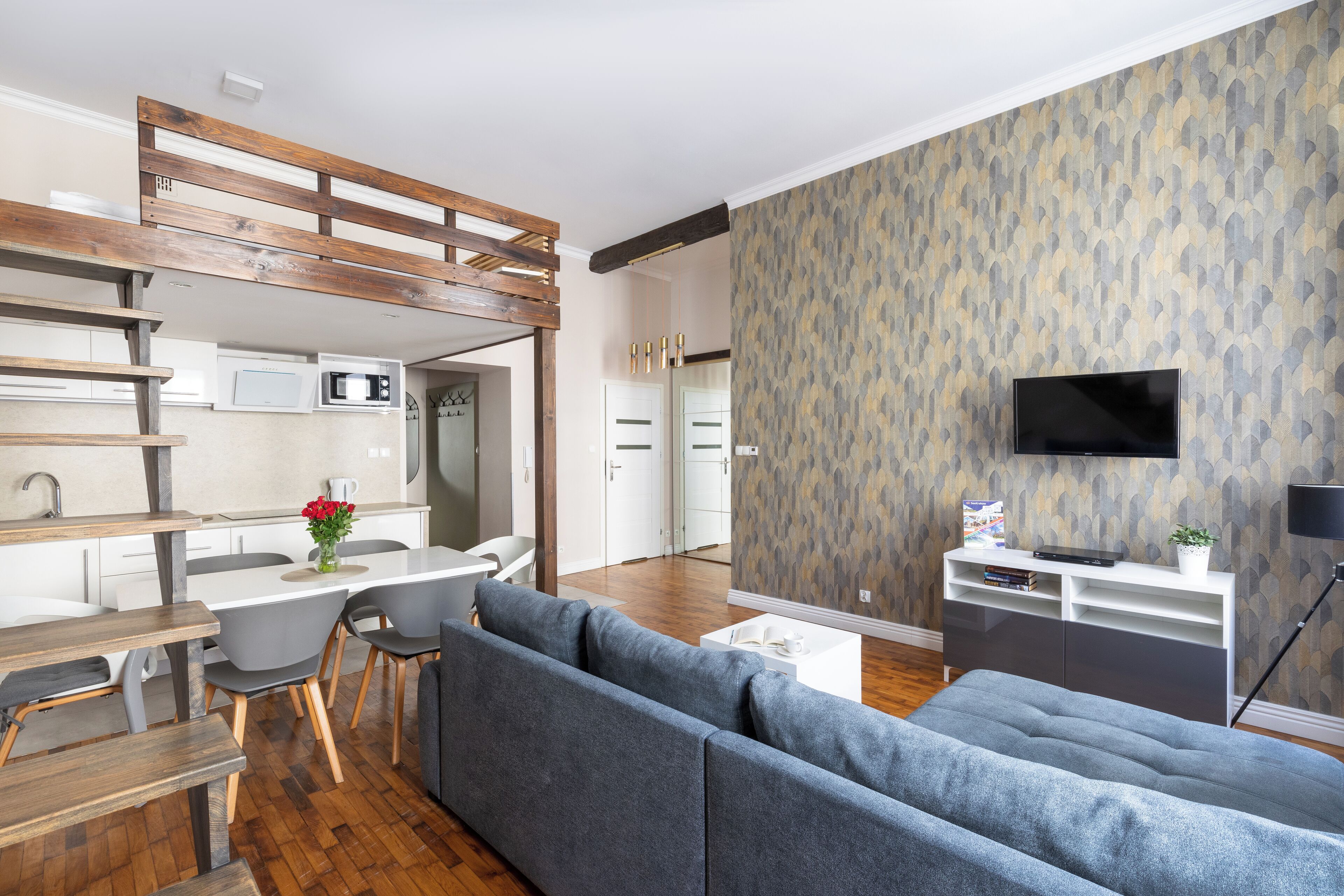 A modern living room with a grey sofa, wooden dining table, and a kitchen area with a microwave.