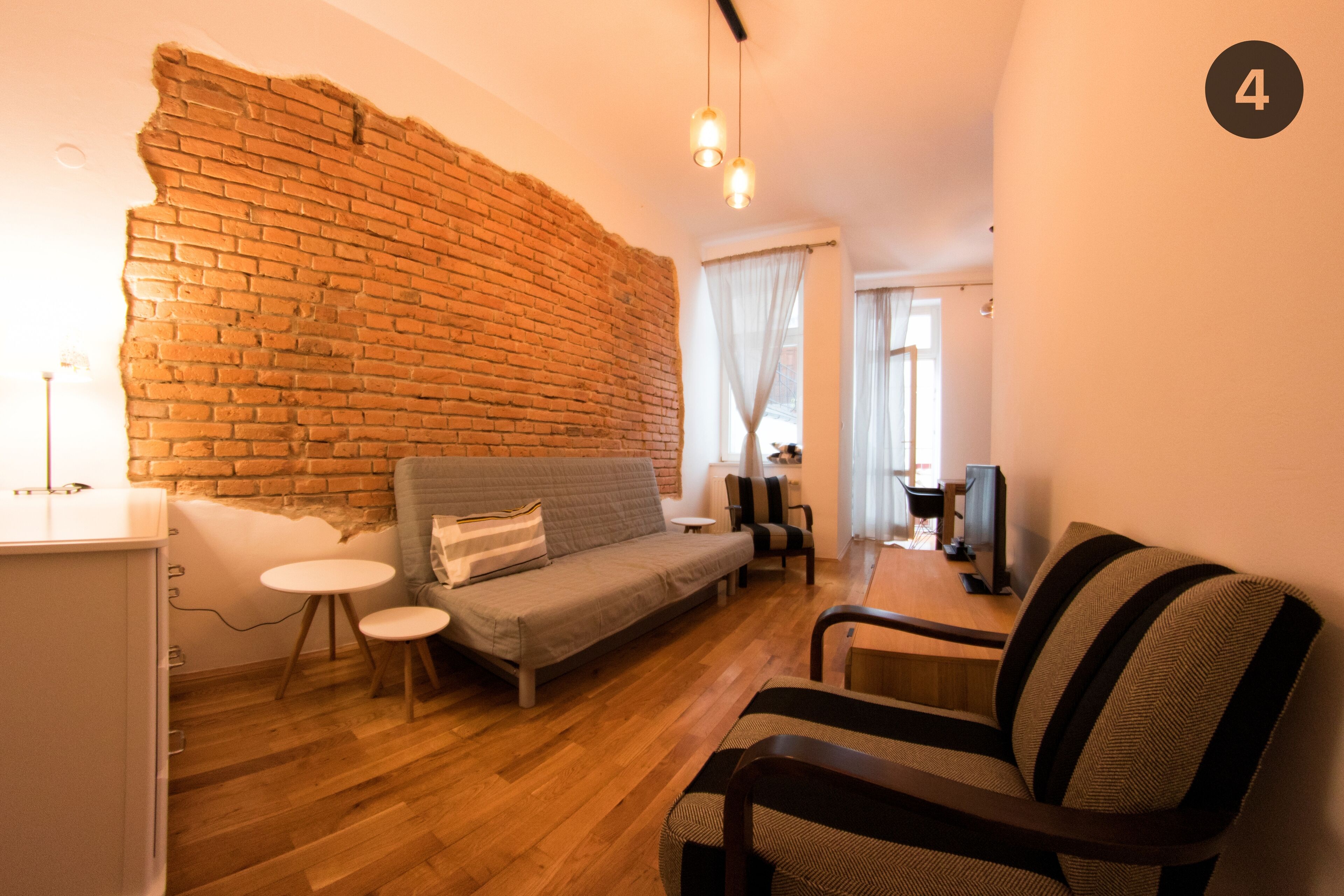 A modern living room with a brick wall, a sofa, a chair, a small table, and a TV.