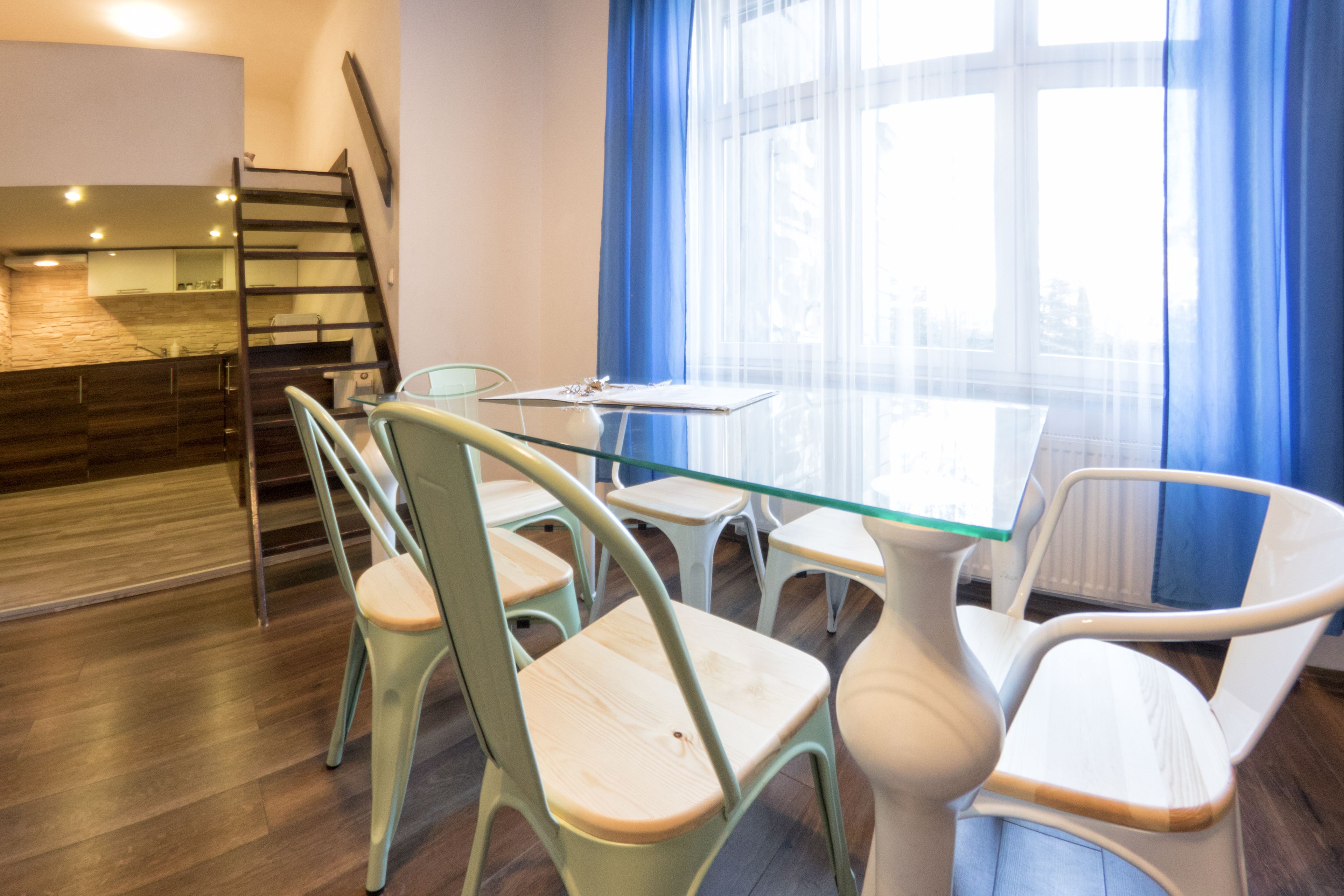 Un comedor moderno con una mesa de vidrio y sillas de metal, una escalera de madera y vistas amplias a través de grandes ventanales.