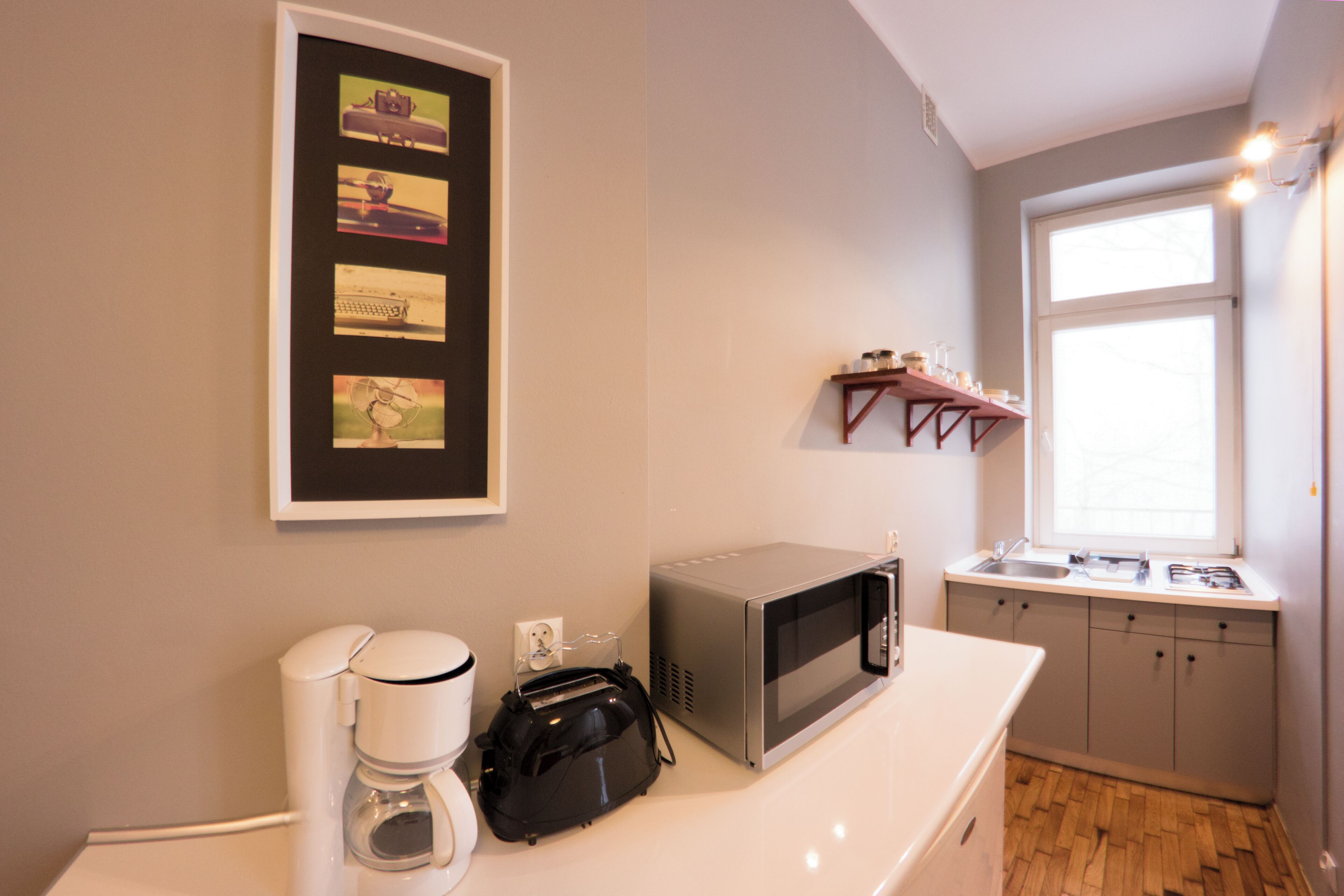 Una pequeña cocina americana equipada con microondas, cafetera y tostadora. Hay un cuadro en la pared y una ventana con vistas al exterior.