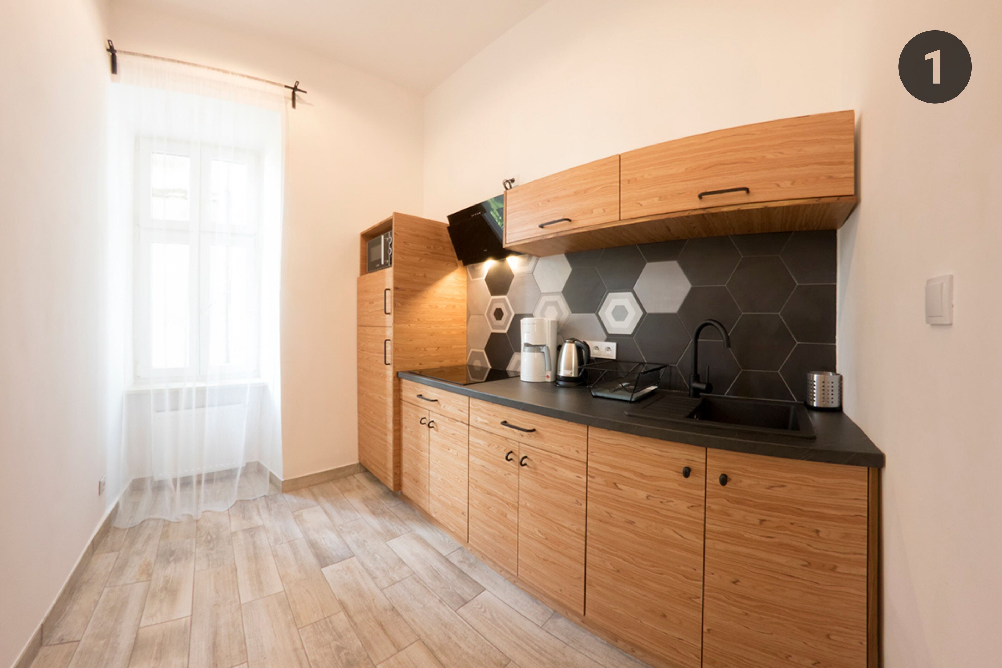 Une cuisine moderne avec des meubles en bois, un plan de travail noir et un pare-feu en carreaux hexagonaux.