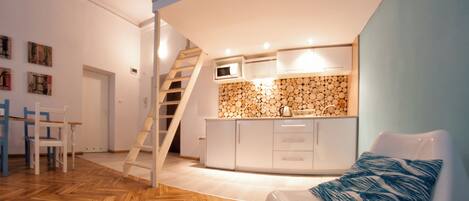 Una cocina moderna con pared de madera rústica, armarios blancos y un microondas integrado. Una silla blanca con un cojín azul está en primer plano.