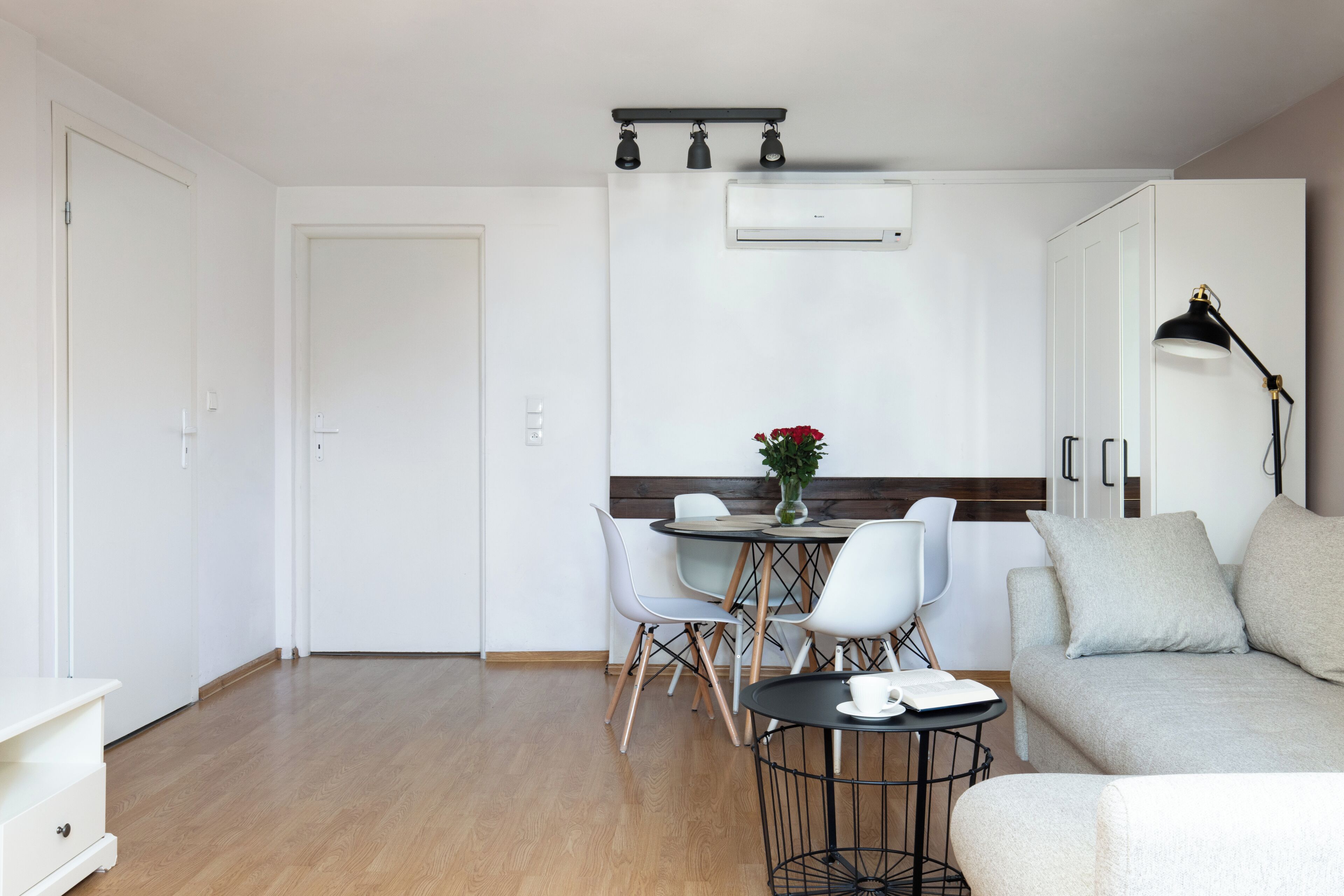A modern, minimalist living room with a sofa, a dining table with chairs, and a small side table with a lamp.