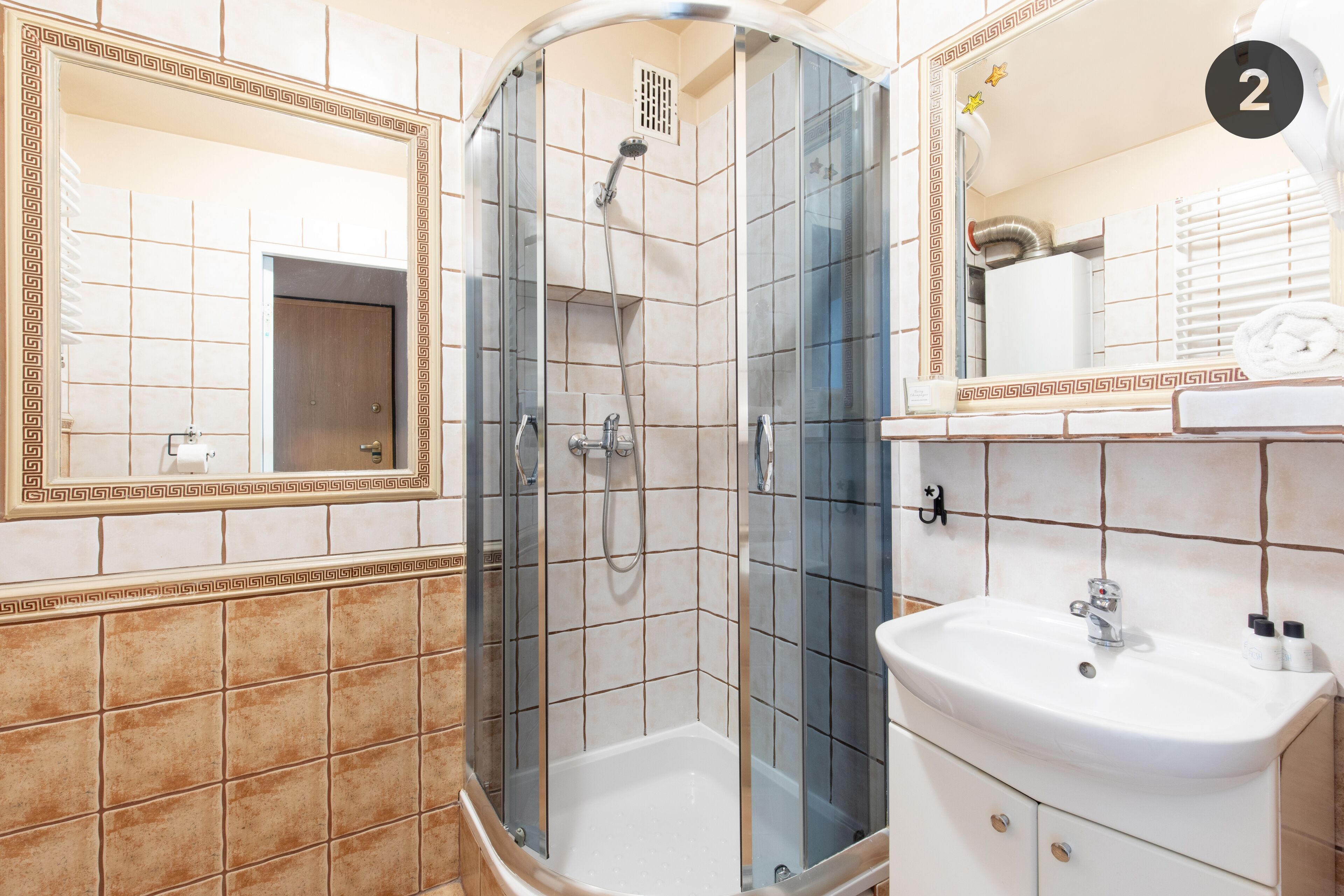 Een badkamer met een douchecabine van glas, een wastafel en een spiegel met decoratieve tegels.