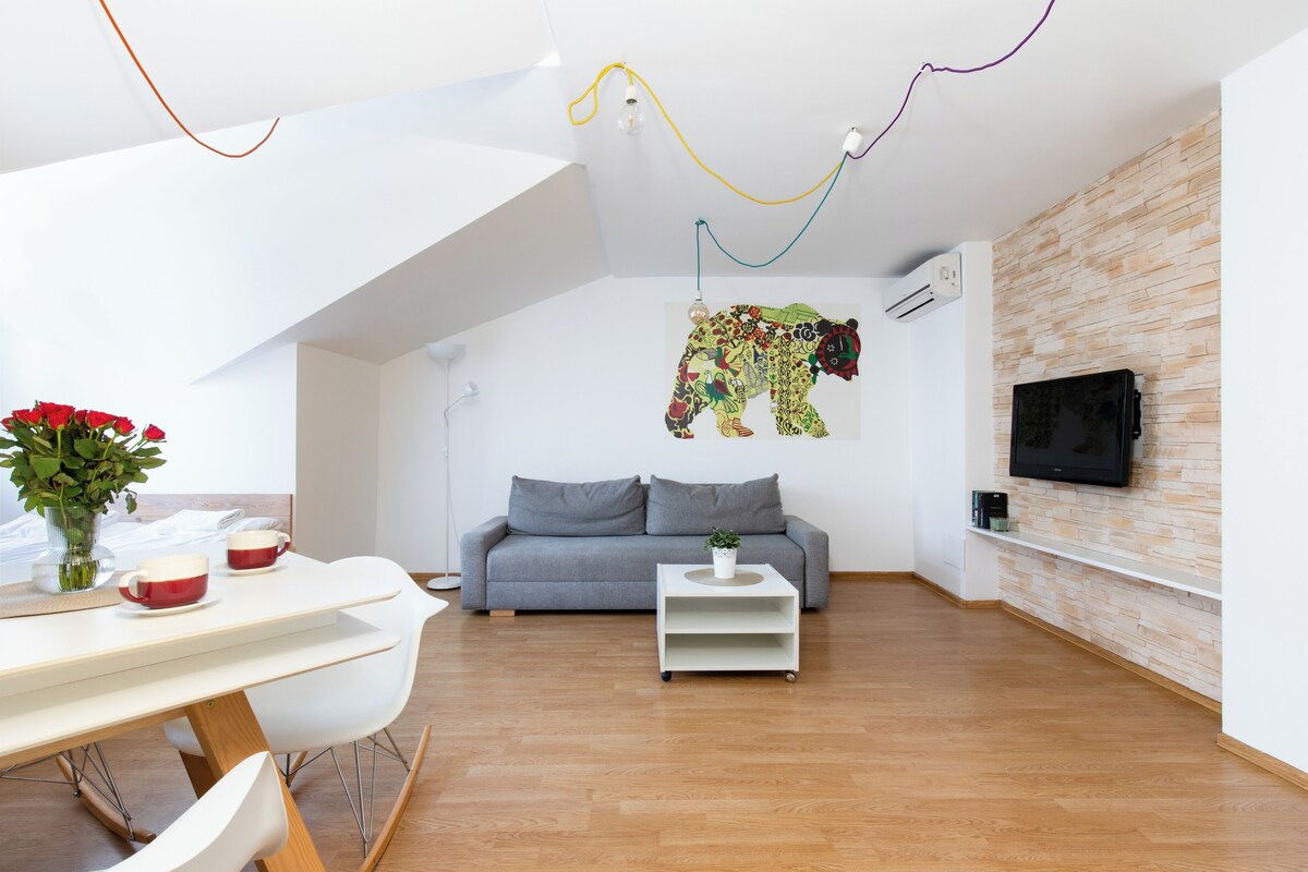 A modern living room with a grey sofa, a white coffee table, and a wall-mounted TV.