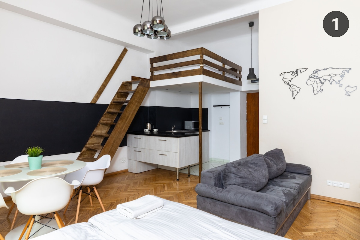 A modern loft-style room with a bunk bed, a kitchenette, a dining area, and a gray sofa.