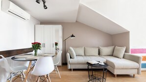 A modern living room with a sofa, dining table, chairs, and a lamp. - Fresh Apartments (Kraków)