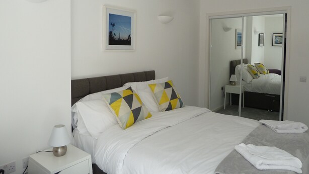A neatly made bed with white bedding and patterned pillows, a bedside lamp, and a framed picture on the wall.