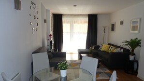 A modern living room with a glass table, two sofas, a coffee table, and a potted plant.
