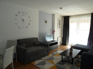 Una sala moderna con un sofá gris, un televisor pequeño y una mesita de centro.