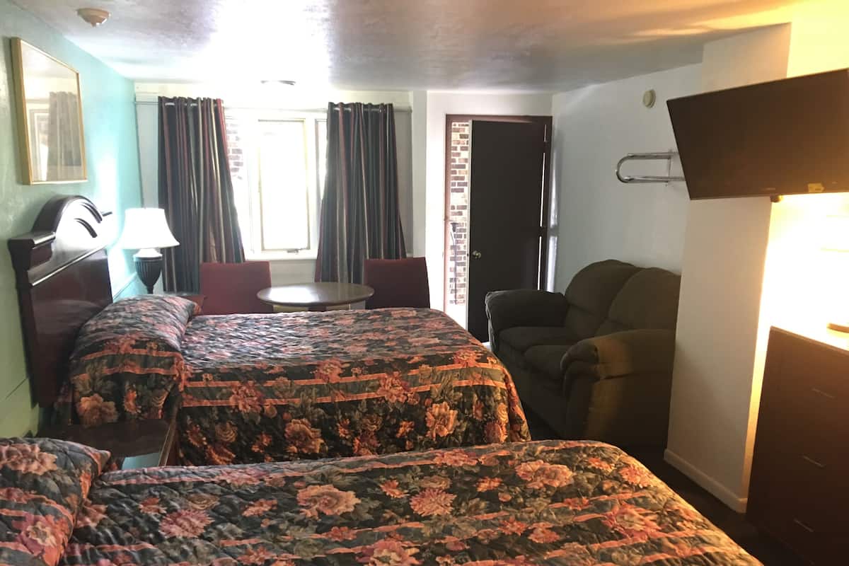 Hotellihuone, jossa on kaksi sänkyä, työpöytä, tuoli, televisio ja ikkuna, jossa on verhot.