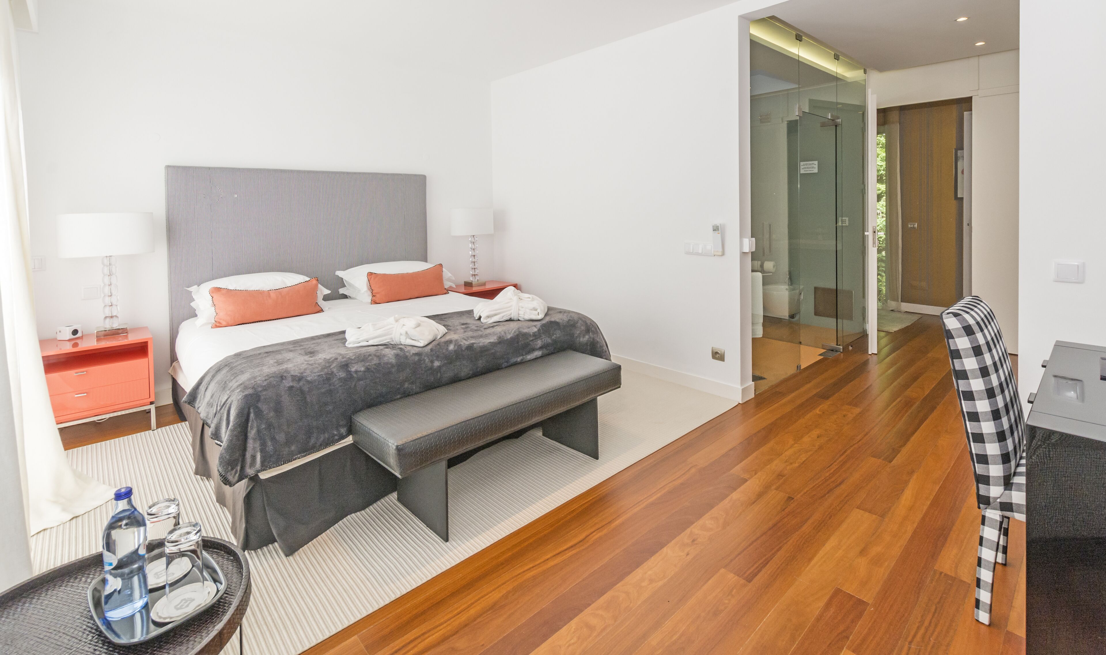 A modern hotel room with a large bed, bedside tables, a bench, and a chair.