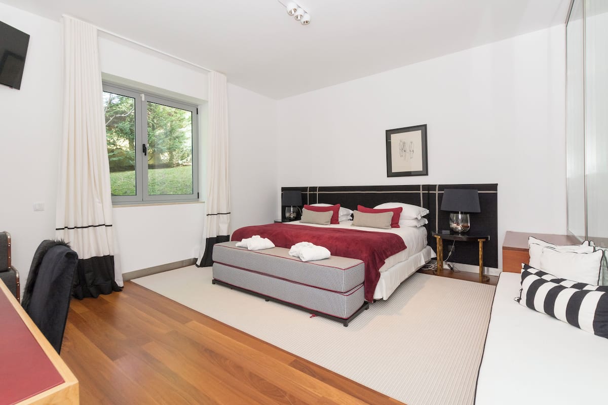 A bedroom with a bed, bedside tables, a desk, a chair, a window with curtains, and a framed picture on the wall.
