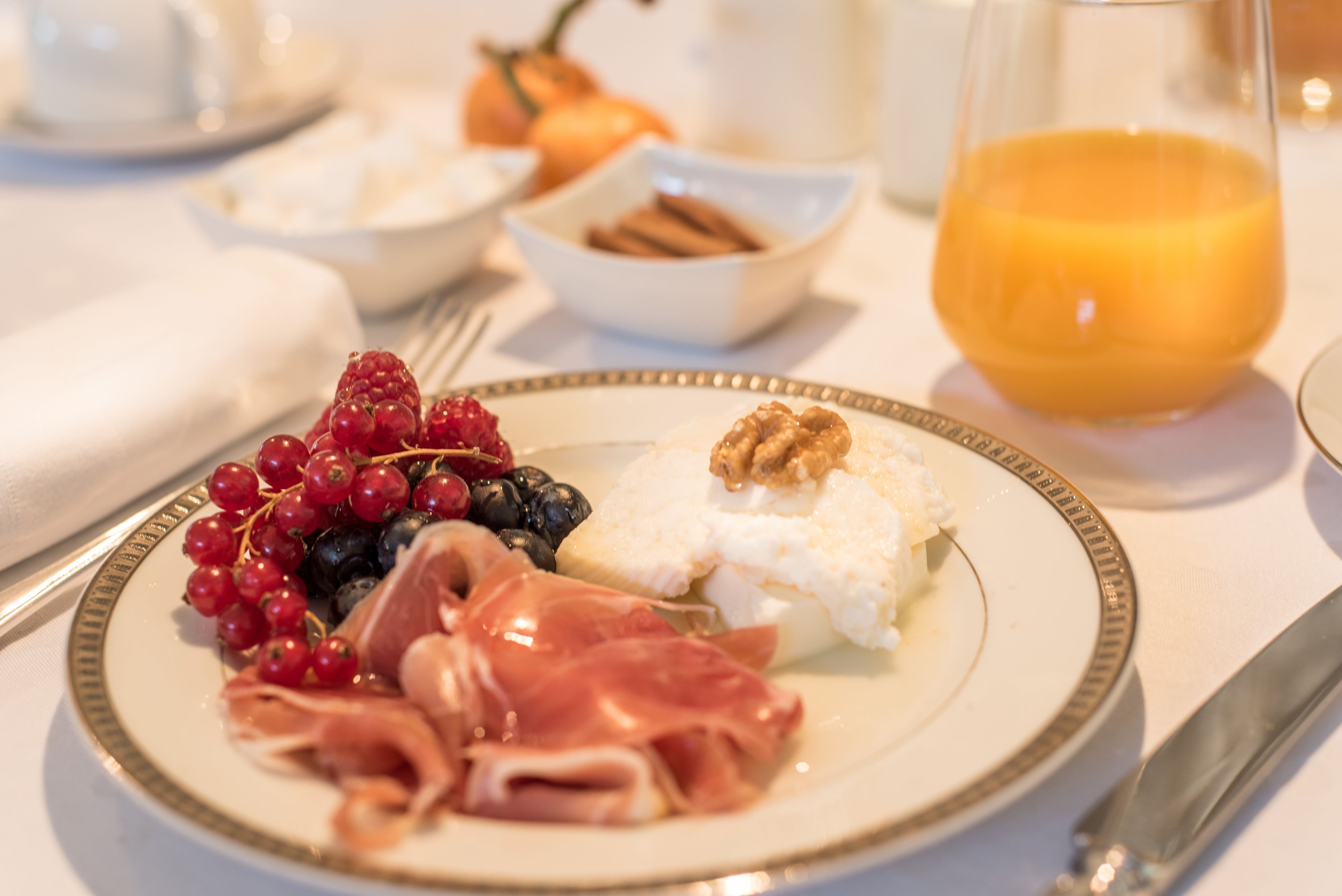 Une assiette de petit-déjeuner avec des fruits, des noix et du fromage, un verre de jus d’orange et un bol de bâtonnets de cannelle.