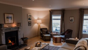 A cozy living room with a fireplace, comfortable seating, a coffee table, and a view of the outdoors. - Hame Hotel (Dunvegan)