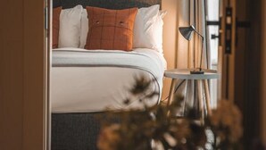 A bedroom with a bed, pillows, a bedside table, and a lamp. - Hame Hotel (Dunvegan)