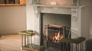 A fireplace with a fire, two green leather stools, and decorative vases on the mantel. - Hame Hotel (Dunvegan)