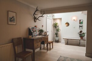 Um quarto acolhedor com uma escrivaninha de madeira, uma cadeira, um radiador, uma planta em vaso e um banco.