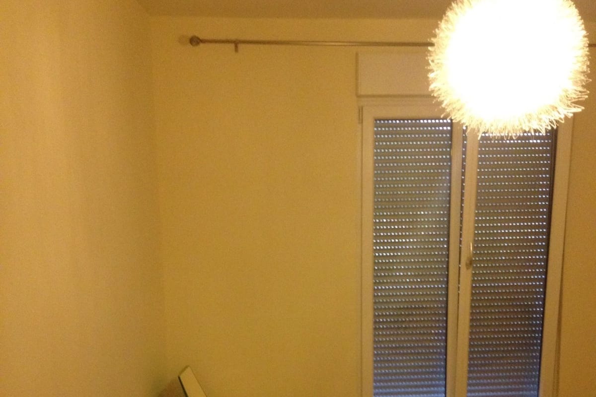Ein Schlafzimmer mit einem Bett, einem Heizkörper, einem Stuhl und einem Fenster mit Jalousien.