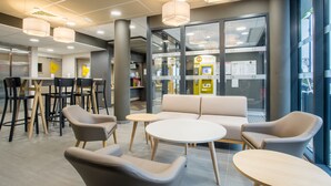 A modern interior with seating areas, tables, and a counter. - B&B HOTEL ANNEMASSE Saint-Cergues (Saint-Cergues)