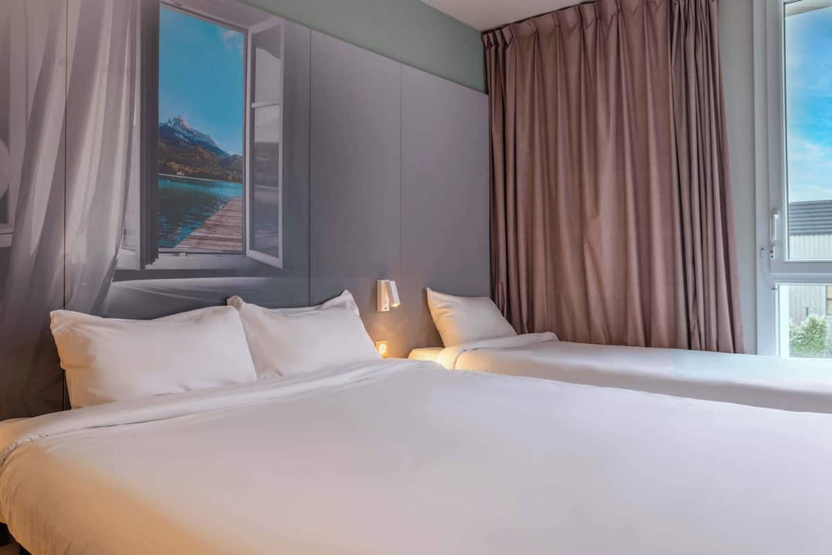 A hotel room with two beds, a large window with curtains, and a view of a mountain and lake.