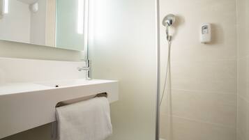 A modern bathroom with a white sink, a towel hanging on the wall, a glass shower enclosure, and a handheld showerhead.