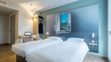 Habitación de hotel con dos camas, un escritorio con computadora, una silla y un ventanal con vistas a la montaña.