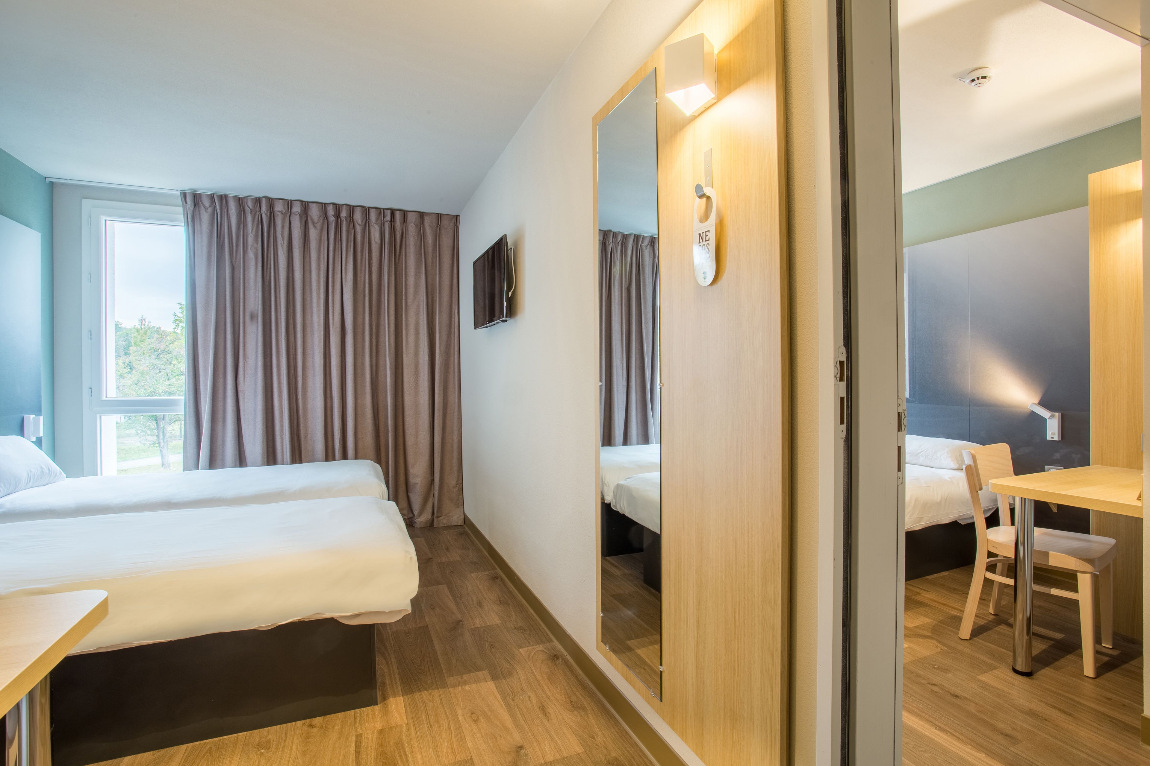 A hotel room with two beds, a desk, a chair, a TV, and a mirror.