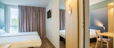 A hotel room with two beds, a desk, a chair, a TV, and a mirror.