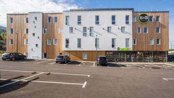 A modern hotel with a flat facade, multiple parking spaces, and a clear sky.