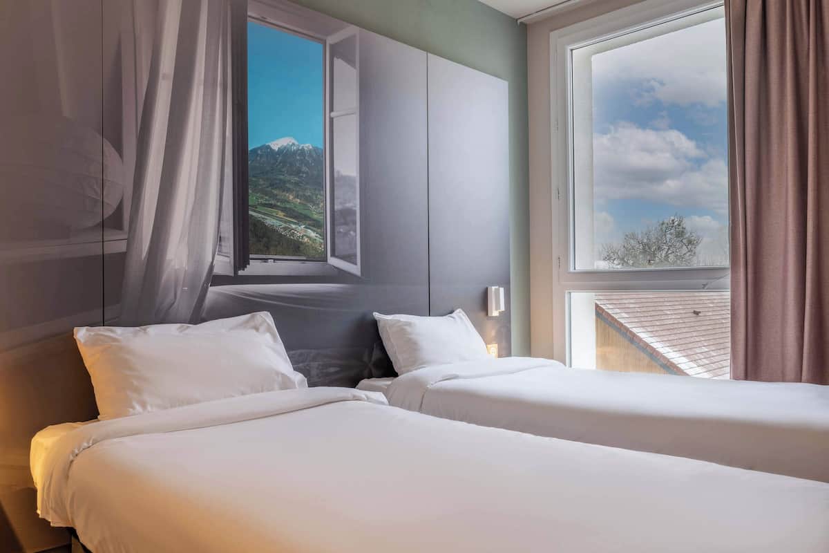 A hotel room with two beds, a large window with a mountain view, and a modern design.